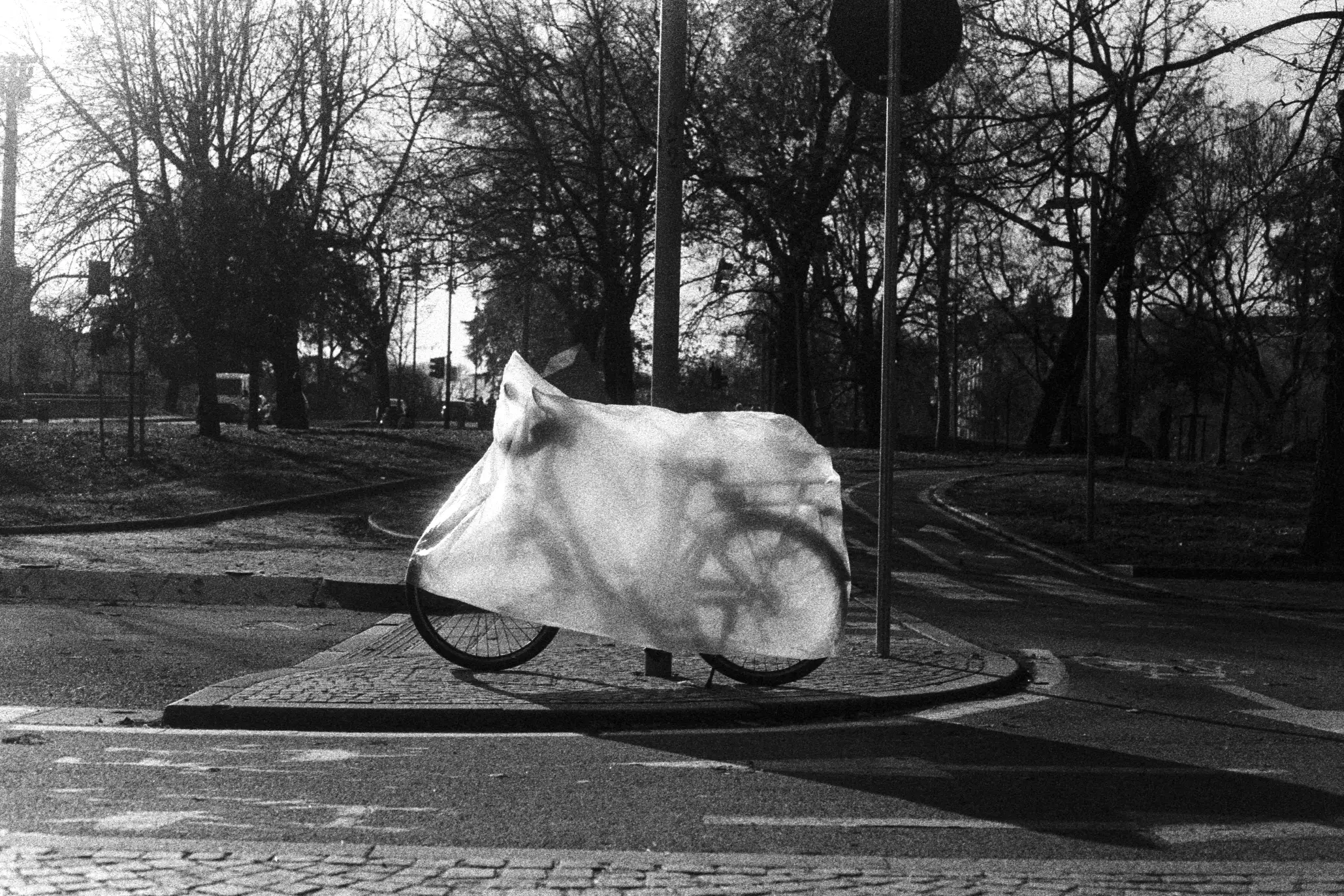A bike covered in a white plastic sheet chained to a pole.
